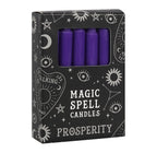 Hand holding a box of purple Prosperity spell candles beside lit candles and dried flowers