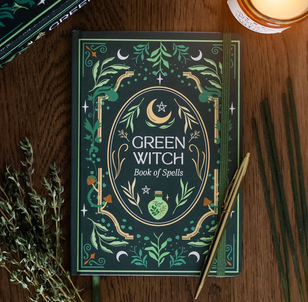 Green Witch Book of Spells journal styled on a wooden desk with a pen, dried herbs, incense sticks and a candle