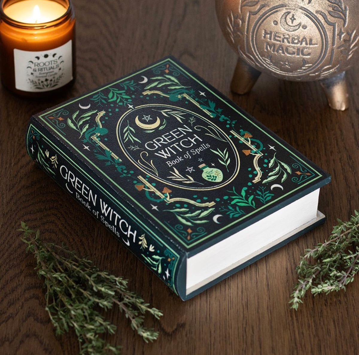 Green Witch Book of Spells box styled on a wooden table with a candle, cauldron and fresh herbs