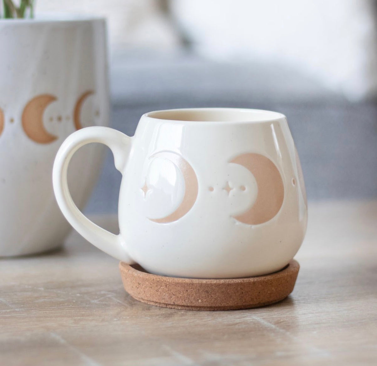 Cream moon phase mug resting on a cork coaster on a kitchen worktop