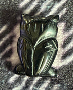 A small carved black cat figurine with a glossy finish, resting on a textured, sparkly black and silver surface.