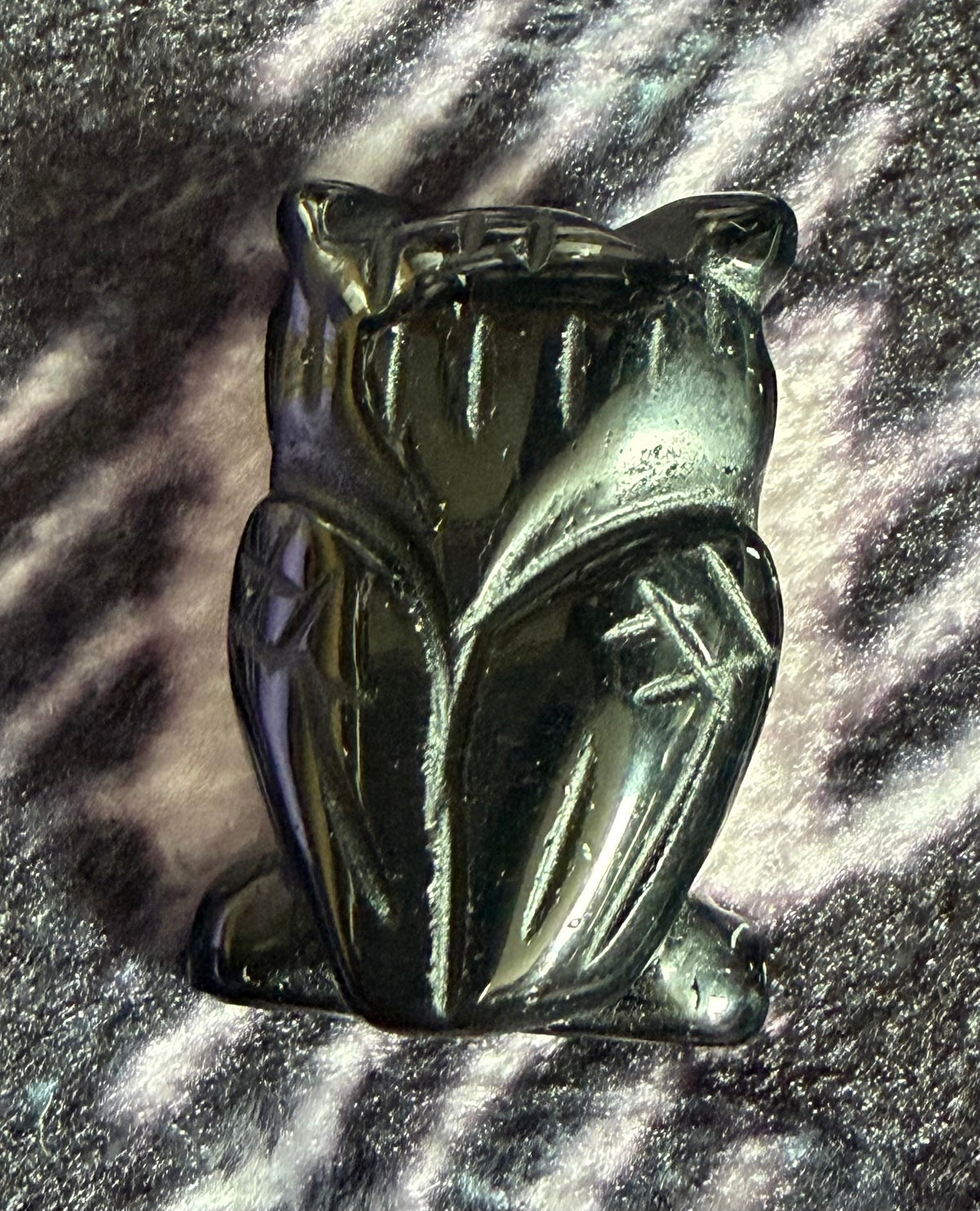 A small carved black cat figurine with a glossy finish, resting on a textured, sparkly black and silver surface.
