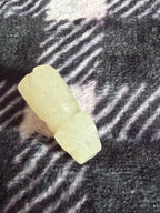 A small pale yellow carved stone or resin figurine placed on a dark textured fabric background with diagonal light reflections.