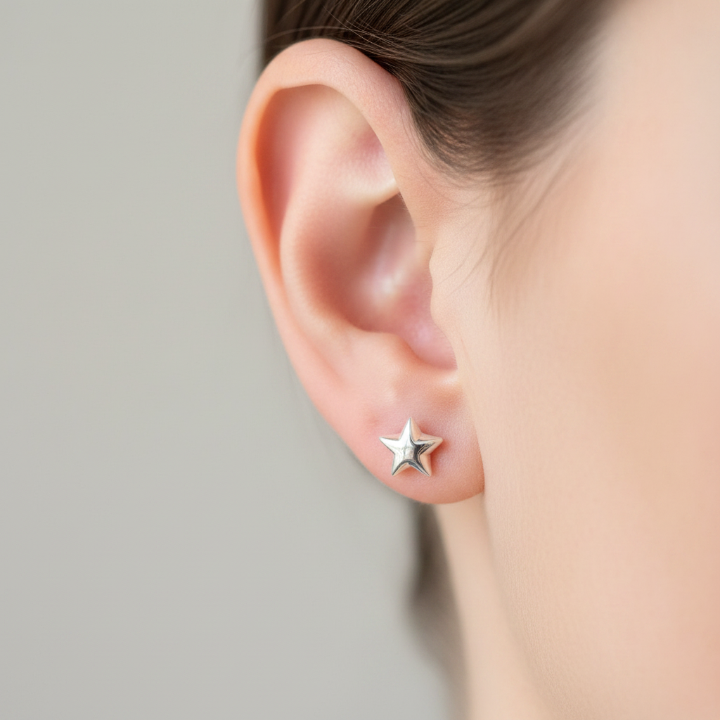 A close-up of a person's ear wearing a small silver star stud earring against a soft light gray background.