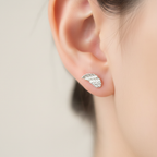 A close-up of a person's ear wearing a small silver leaf stud earring with tiny clear stones along the lower edge.