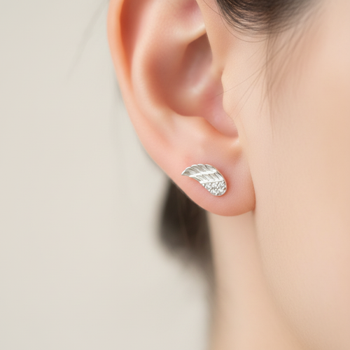 A close-up of a person's ear wearing a small silver leaf stud earring with tiny clear stones along the lower edge.