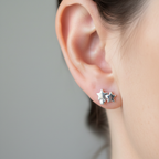 A close-up of a person's ear wearing a pair of silver star-shaped stud earrings against a soft gray background.