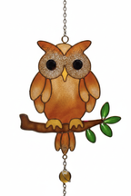 Close up detail of stained glass style amber owl perched on branch with green leaves, glittery eyes