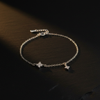 Sterling silver dual CZ star bracelet laid on a dark moody surface with soft dramatic lighting, showing two four-pointed star charms on a fine cable chain
